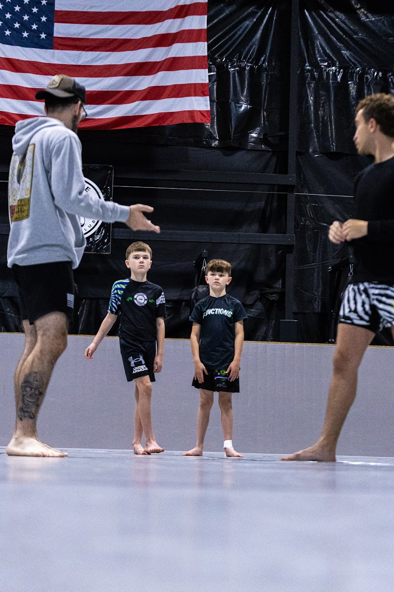 Coach instructing two young students on the mat in front of an American flag